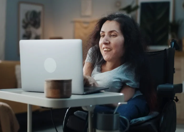 Disabled woman in wheelchair looking at laptop and smiling