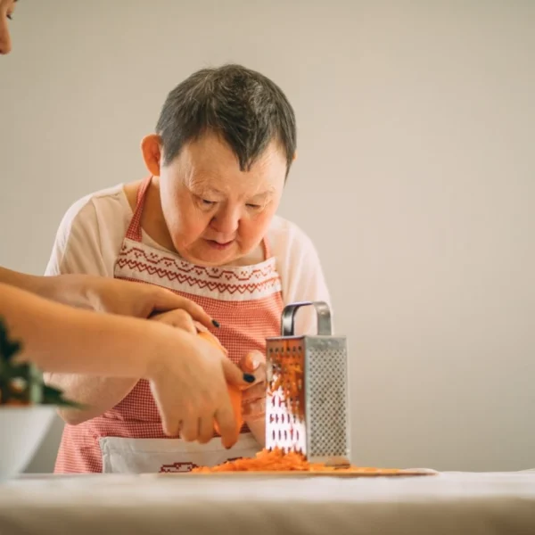 Disabled woman grating carrots with carer