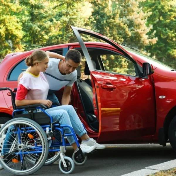 Carer helping woman in wheelchair into car