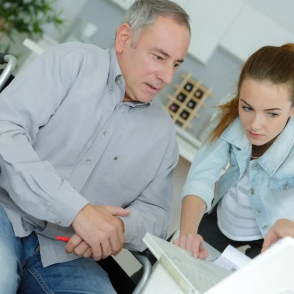 Carer pointing to laptop showing man in wheelchair
