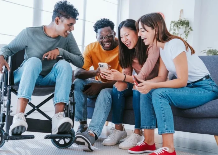 Disabled man in wheelchair with group of friends laughing at something on a mobile phone